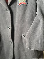 Close-up of the coat front buttons, crest patch on left chest, and fraying at sleeve edge