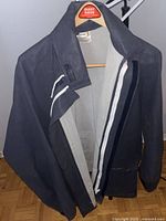 Front and side view of vintage navy blue waterproof coat on hanger against grey wall and wooden floor.