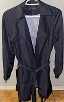 Front view of navy blue Zara basic trench coat hanging on a hanger showing collar, front opening, and belt.