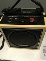 Front view showing the speaker grill, carrying handle, and part of the control panel including track buttons and volume control.