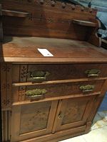 Front view of antique wooden cabinet showing two drawers with brass handles and carved floral motifs above double doors also with carved floral panels.