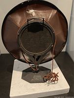 Front view of the antique radio speaker showing the protective wire mesh and cloth-covered cable coiled on the stand base.