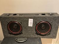 Image of rectangular gray carpeted speaker enclosure with two round speakers featuring red rings and black protective grilles.