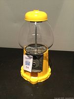 Photo of a single yellow candy dispenser with clear globe top and metal coin slot mechanism.