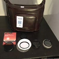 Brown Canon FD Lenses carrying bag with five lens filters and cases arranged on a table.