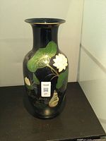 Front view of the black ceramic vase showing detailed hand-painted green leaves and white flowers with gold accents.