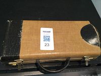 Closed view of the brown vintage clarinet case with black corner reinforcements, handle, and brass clasps.