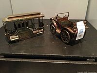 Two copper and tin music box toys including a vintage bus and a vintage car placed on a dark surface.