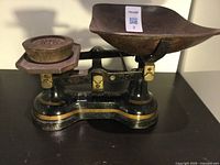 Front and top view of cast iron scale showing curved pan, balance arm, and attached brass weight.