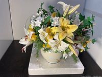 Front view of faux flower arrangement showing yellow and white lilies and green ivy in yellow ceramic pot.