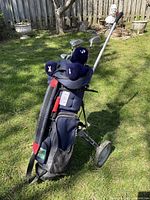 Overall side view of golf club set in bag on push cart on grass with headcovers visible