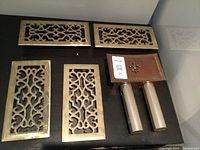 4 brass air register covers with intricate scrollwork and 2 door bell units displayed on black background