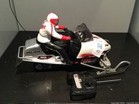 Remote controlled Polaris snowmobile toy with rider figurine and black radio controller on a flat surface