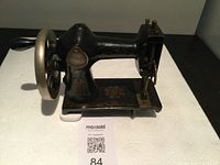 Full side view of the black antique sewing machine, showing hand-crank wheel and decorative patterns.