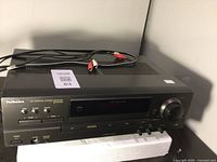 Black Technics SA-EX140 AV control stereo receiver with RCA cables on top, photographed from front-left angle on white padding.