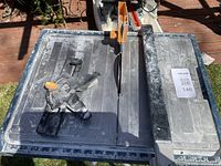 Top view showing cutting blade, adjustable clamp, and measurement rulers on the tile cutter surface.