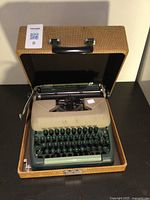 Vintage typewriter with green keys and beige upper panel in a brown carrying case with black handle, photographed from the top.