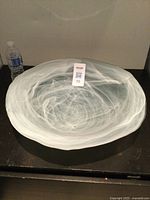 Top view of a large hand made glass bowl showing swirling white pattern on black surface with water bottle for scale.