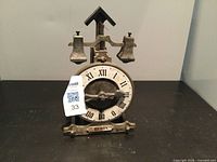 Front view of vintage windup clock showing dial with Roman numerals and twin bells overhead.