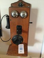 Front view of vintage wooden crank wall telephone showing dual metal bells, mouthpiece, and earpiece hook.