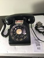 Black vintage rotary dial telephone with emergency 911 label and power cord.