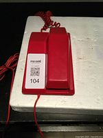 Side view of the red rotary phone showing handset laying on white foam base.