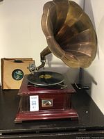 Full view of gramophone showing brass horn, wooden base and stack of record sleeves.