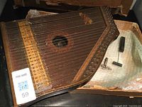 Overall view of the vintage wooden zither with multiple strings and decorative surface, showing included tuning tools in packaging.