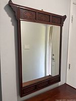 Front view of the antique carved wood wall mirror mounted on wall, showing intricate carved designs on top and bottom frame sections.
