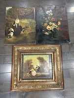 Three oil paintings laid on floor showing dog scene, floral painting, framed genre scene