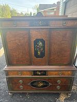 Full front view of antique wooden desk showcasing wood grain panels and hand-painted floral designs on central vertical panel and drawers.