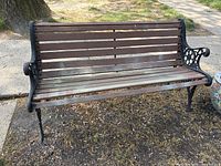 Front view of classic outdoor bench showing wooden seat and back with cast iron armrests and legs in a decorative style.