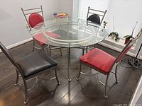 Photo of the round glass dining table and four chairs showing the overall appearance and chair color variation.