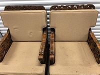 Top view of two wooden chairs with beige cushions showing the carving patterns and fabric texture with some stains.
