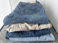 Folded stack of four pairs of denim jeans showing blue and beige colors
