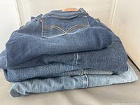 Stack of five pairs of blue denim Levi's jeans showing different shades of blue from dark to light.