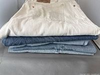 Stack of five pairs of Levi's jeans showing a range of denim colors from white to darker blues
