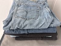 Stack of five jeans showing blue and black colors with visible back pocket stitching.