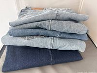 Stack of five folded Levi's denim jeans in blue shades from light to dark wash, showing the jeans stacked horizontally.