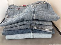 Stack of five pairs of medium blue denim jeans showing different wash levels and pocket stitching