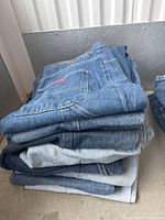 View of stacked 10 pairs medium blue denim jeans with visible waistband and pockets