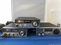 Three vintage CB radios including Pearce-Simpson Puma 23C, General Electric KSV 7901, and General Electric 40 Channel P.L.L System, arranged on a table.