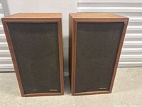 Pair of vintage Realistic speakers standing upright showing front with black fabric covers and wood frames.