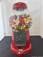 Front full view of vintage red metal and glass gumball machine filled with colorful gumballs.