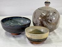 Three art pottery pieces by Richard Trost on white background: smaller speckled bowl, blue glazed bowl, and large covered jar with crackle glaze.