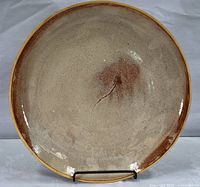 Front view of the round tan and brownish-red pottery platter displaying center crack and speckled glaze
