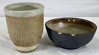 Photo showing side-by-side view of the vase and bowl on a white surface, highlighting the textured finish and glaze on the vase and the dark bowl with holes at the rim.