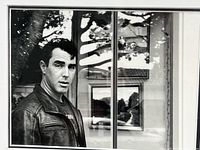 Close-up photo of the black and white image showing a man in a leather jacket near a window with reflections, signed by Richard Trost