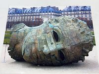 Full view of the large bronze sculpture photo print showing the sculpture lying horizontally outdoors with a detailed background of buildings.