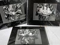 Three black matted black and white photo prints in poly sleeves showing hands holding fruit and decorative bowl